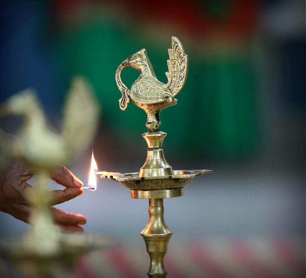 A hand lights a traditional brass lamp in an Indian ritual, focus on flame and lamp.